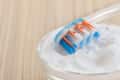 Toothbrush with blue and orange bristles resting in a glass bowl of white powder on a wooden surface.