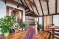Loft-style living room with exposed beams, wooden floors, large potted plants, and a colorful rug leading to a seating area.