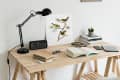 Wooden desk with a lamp, digital clock, open book, notebooks, glasses, and a bird illustration.