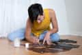 Person in yellow tank top painting on dark fabric pieces on wooden floor.