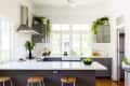 Modern kitchen with gray cabinets, white countertops, bar stools, potted plants, and a bowl of green apples.