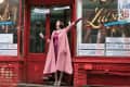 Woman in pink coat and hat joyfully posing outside Lutzi's Butcher Shop with vintage signage.