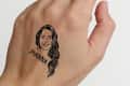 Hand with a temporary tattoo of a woman's face and the name "Joanna" on the back.