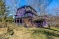 Victorian-style purple house with green shutters surrounded by bare trees and shrubs.