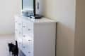 White dresser with TV on top, black cat walking beside it, wooden beams on ceiling.