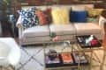 Beige sofa with colorful pillows, brick wall, round mirror, gold coffee table, and geometric rug in a cozy living room.