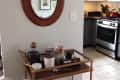 Bar cart with glassware and decor under oval mirror near kitchen with stove and red kettle.