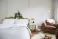 Bedroom with white bedding, pine garland on headboard, brown leather armchair, and gold lamp on a side table.
