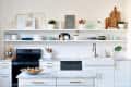Modern kitchen with white cabinets, marble countertops, open shelves, colorful dishes, and a black stove.