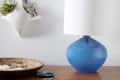 Blue ceramic table lamp with white shade on wooden surface, next to a wall-mounted planter with air plants.