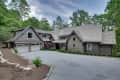 Rustic stone and wood house with gabled roof, two-car garage, and landscaped driveway surrounded by trees.