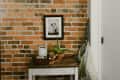 Small wooden table with a typewriter, potted plant, and framed photo against a brick wall.