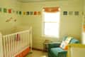Nursery with white crib, teal armchair, colorful wall art, and a window with a peach curtain.