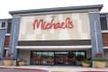 Entrance of Michaels store with large red sign, beige and gray facade, and potted plants by the doors.