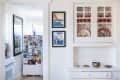 Kitchen with a fridge covered in photos, floral-patterned cabinet, and framed art on the wall.