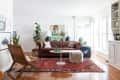 Living room with brown leather sofa, red patterned rug, wicker chair, and large plant, featuring a globe and artwork.