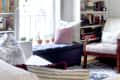 Cozy living room with bookshelves, a navy ottoman, white armchair, and potted plants by a window.