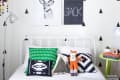 Kids' bedroom with triangle wall pattern, white bed, colorful pillows, fox plush toy, and green side table with books.