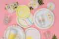 Colorful paper plates and cups with daisy patterns on a pink surface, surrounded by fresh daisies.