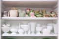 Cabinet with vintage green and white glassware, including vases, bowls, and a rooster-shaped dish.