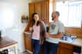 Couple laughing in a kitchen with wooden cabinets, orange tiles, and a knife rack on the wall.
