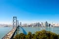 Bay Bridge leading to San Francisco skyline with clear blue sky.