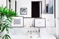 Modern bathroom with a white marble tub, large mirror, framed art, and a potted plant.