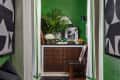 Hallway with green walls, black and white art, dark tiled floor, wooden cabinet, and plants.