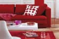 Red sofa with polka dot pillow, white coffee table with books, glass, and bowl of strawberries in a modern living room.
