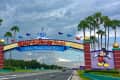 Walt Disney World entrance with Minnie and Mickey Mouse signs, palm trees, and colorful flags.