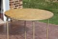 Round folding table with metal legs on a brick patio near a brick wall and grassy yard.