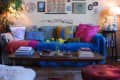Cozy living room with colorful cushions, gallery wall, wooden coffee table, and a lamp on a side table.