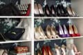 Shoe closet with floral wallpaper, featuring various high heels and handbags on white shelves.