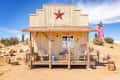 Rustic wooden cabin with a red star, rocking chairs, and an American flag in a desert setting.