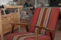 Vintage armchair with red and striped upholstery, wooden arms, and legs in a workshop setting.