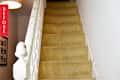 Carpeted staircase with worn white banister and framed photos on the wall.