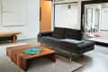 Modern living room with vaulted wood ceiling, black sofa, wooden coffee table, and large windows overlooking a patio.