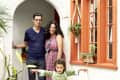 Family standing in a colorful patio with potted plants and a child in a green dress, smiling under an archway.