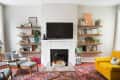 Living room with a wall-mounted TV, white fireplace, wooden shelves, yellow sofa, and patterned rug.