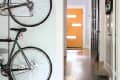 Two bicycles mounted on a wall in a hallway with a striped rug and a view of an orange front door.