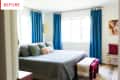 Bedroom with blue curtains, gray bedspread, green pillows, red bench, and abstract wall art.