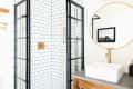 Bathroom with glass shower, white subway tiles, round mirror, and gold fixtures.