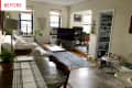 Living room with white sofa, wooden coffee table, TV, plants, and dining table with laptop and potted plant.