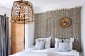 Wicker pendant light over bed with patterned pillows, textured wall hanging, and wooden door in cozy bedroom.