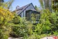 Tudor-style house with dark trim surrounded by lush greenery and tall trees.