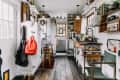 Cozy kitchen with wooden floors, open shelves, a cat on the counter, and a red backpack hanging by the door.