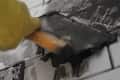 Applying black grout to white subway tiles with a trowel.