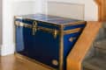 Blue storage trunk with brass accents under a staircase with wooden railing and carpeted steps.