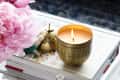 Lit candle in a gold holder on a marble tray with pink flowers, books, and a glass jar of matches.