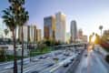 Downtown Los Angeles skyline with palm trees and busy freeway at sunset.